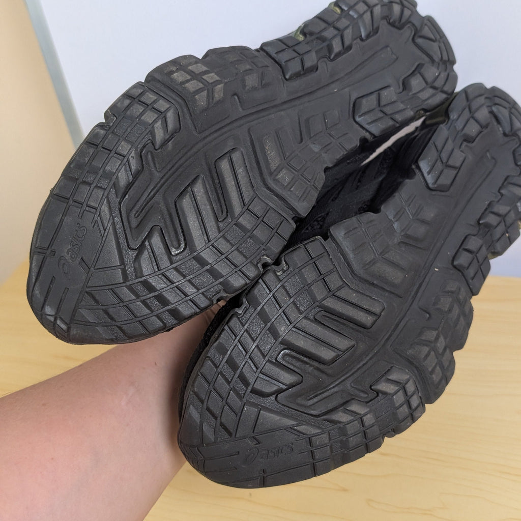 Black shoes with textured sole held by a hand on a light wooden surface.