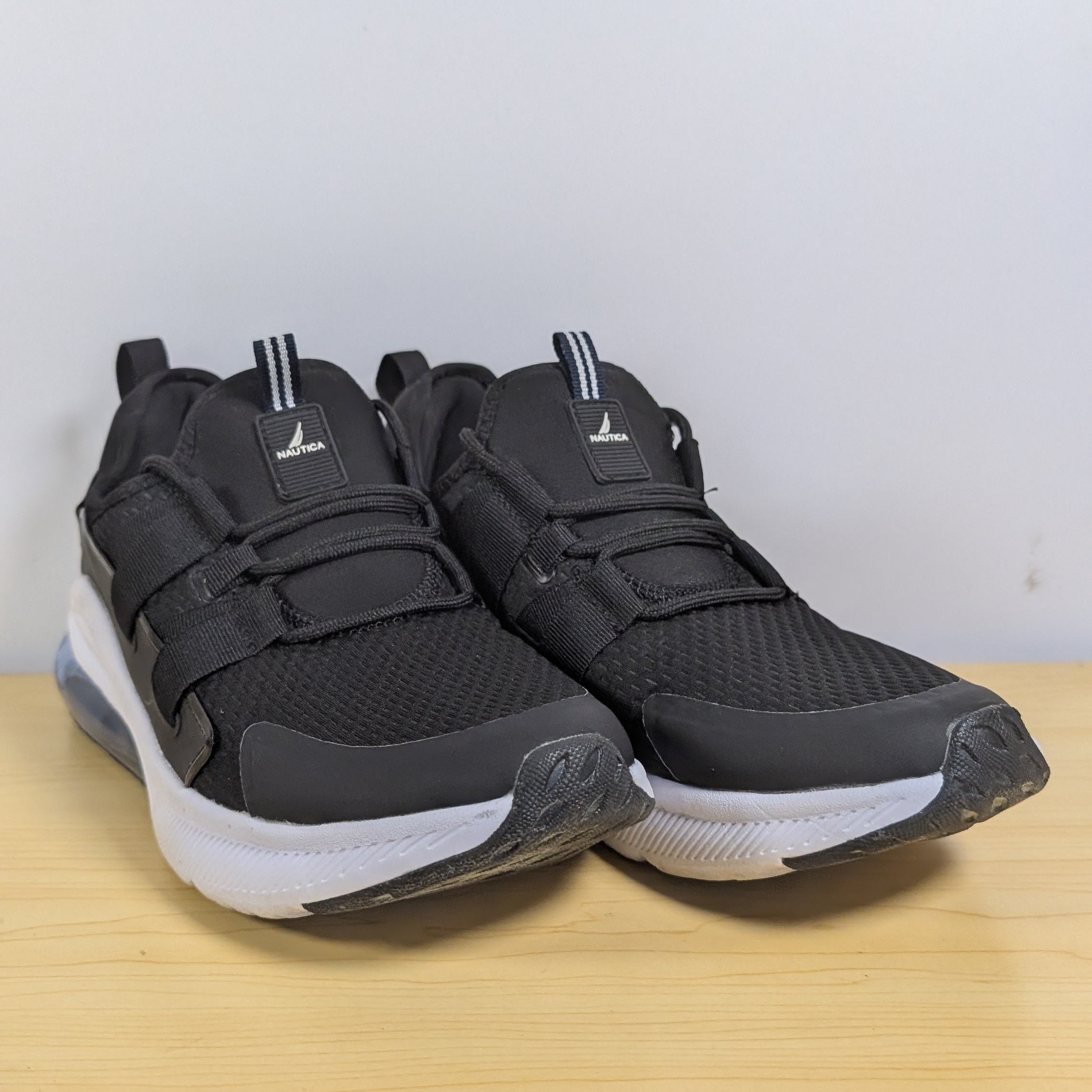 Black athletic shoes on a wooden surface with a light gray background