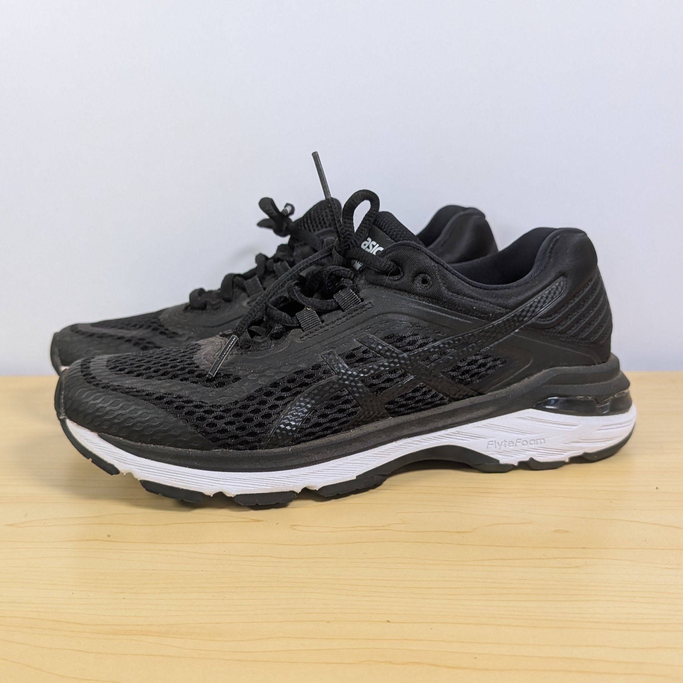 Black running shoes on a wooden surface with a light gray background
