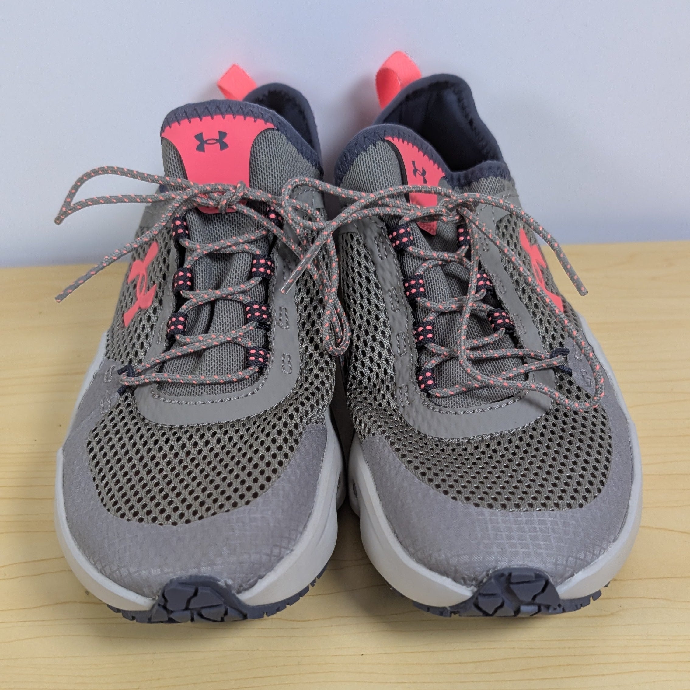 Pair of gray sneakers with pink accents on a wooden surface.